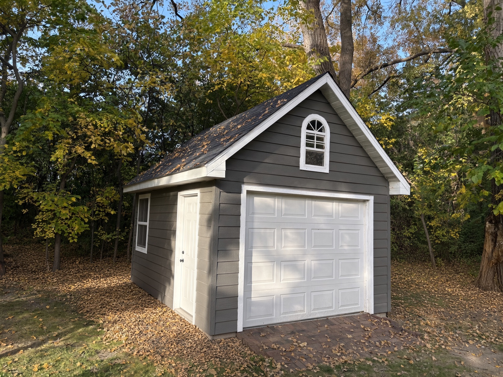 Gray shed with white garage door and trim, finished in the woods